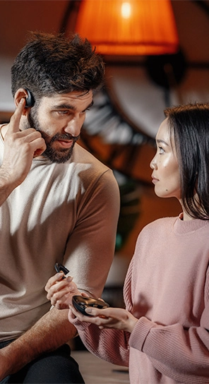 Un homme portant l'écouteur Vasco Translator E1, debout à côté d'une femme tenant l'appareil E1, mettant en avant ses haut-parleurs puissants et son microphone intelligent.