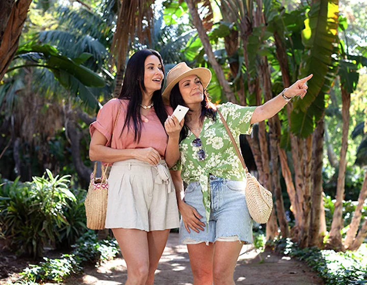 Deux femmes en vacances regardent dans la direction que l'une d'elles indique. L'une d'elles tient un Vasco Translator V4 à la main.