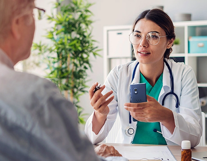 Une femme médecin tenant le traducteur Vasco V4 et s'adressant à un patient pendant une consultation.