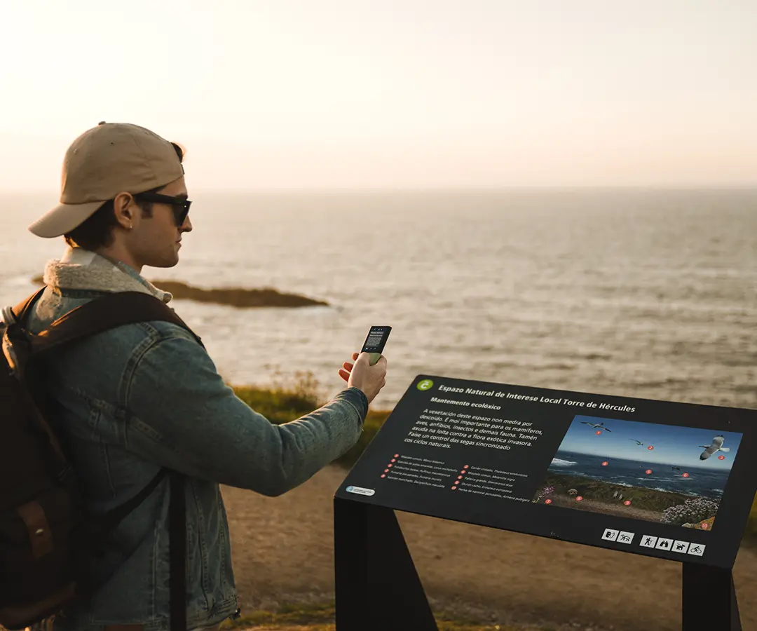 Un homme au bord de la mer utilise un traducteur photo pour lire un panneau contenant des informations touristiques sur son emplacement